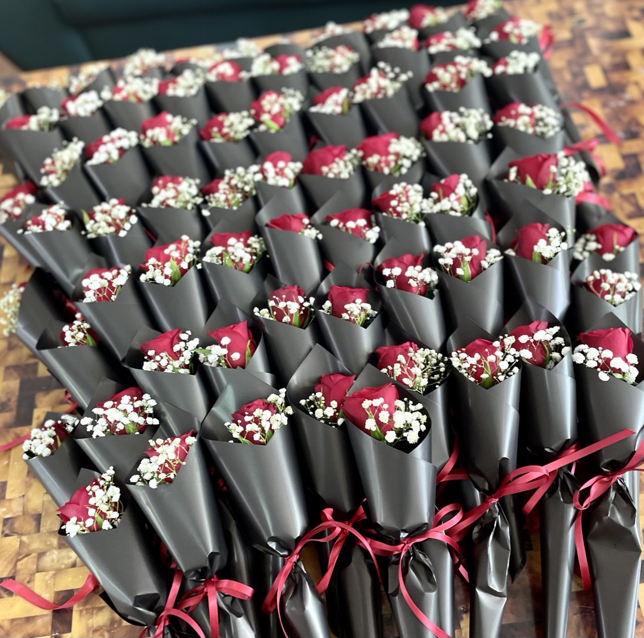 Bulk order of fresh single-stalk red rose bouquets, accompanied by fresh white baby's breath, wrapped in matte black wrapping paper 