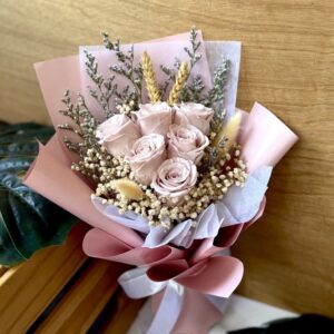 Bouquet of preserved pink roses with accompanying dried filler florals, wrapped in pink