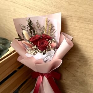 Bouquet of preserved red roses with accompanying dried filler florals, wrapped in pink