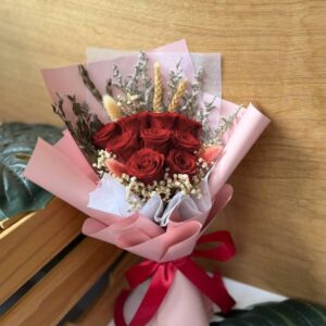 Bouquet of preserved red roses with accompanying dried filler florals, wrapped in pink