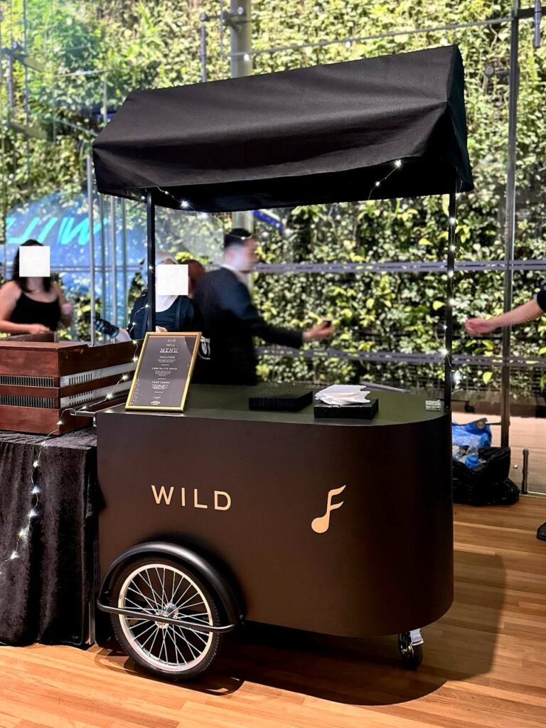 Black mobile pushcart with canopy roof, customised Fatfreq logo in gold. Comes with large storage compartment. Fully customisable from cart body wrapping, simple logo customisation to printing of logo on the cart roof. Our pushcart is available in both black and off white. Perfect for reception tables, product displays, coffee cart, flower bars, or as a centerpiece to any event.