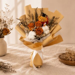 A graduation bouquet featuring preserved burnt orange roses, cotton blooms, dried florals, and a mini graduation bear! Warm, cheerful, and full of sunshine — perfect for congratulating your favourite graduate.