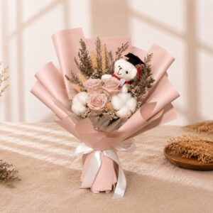 A graduation bouquet featuring preserved pastel pink roses, cotton blooms, dried florals, and a mini graduation bear! Soft, elegant, and timeless — a beautiful keepsake for their special day.
